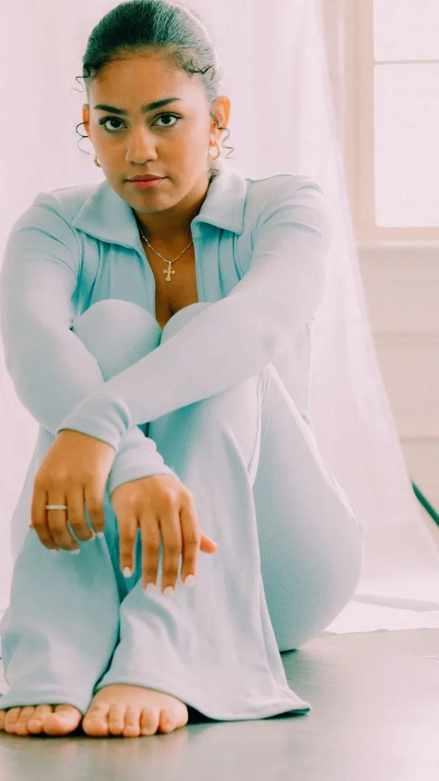 Woman in a pale blue outfit seated beside a bright window
