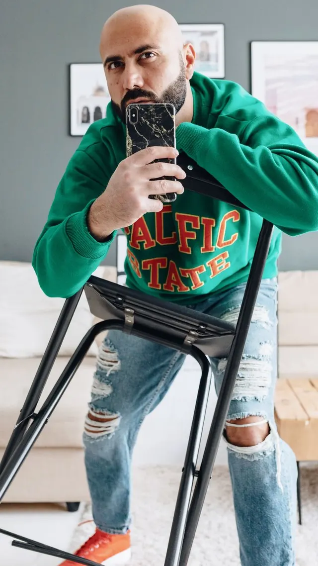 Man in a green sweatshirt taking a mirror photo at home