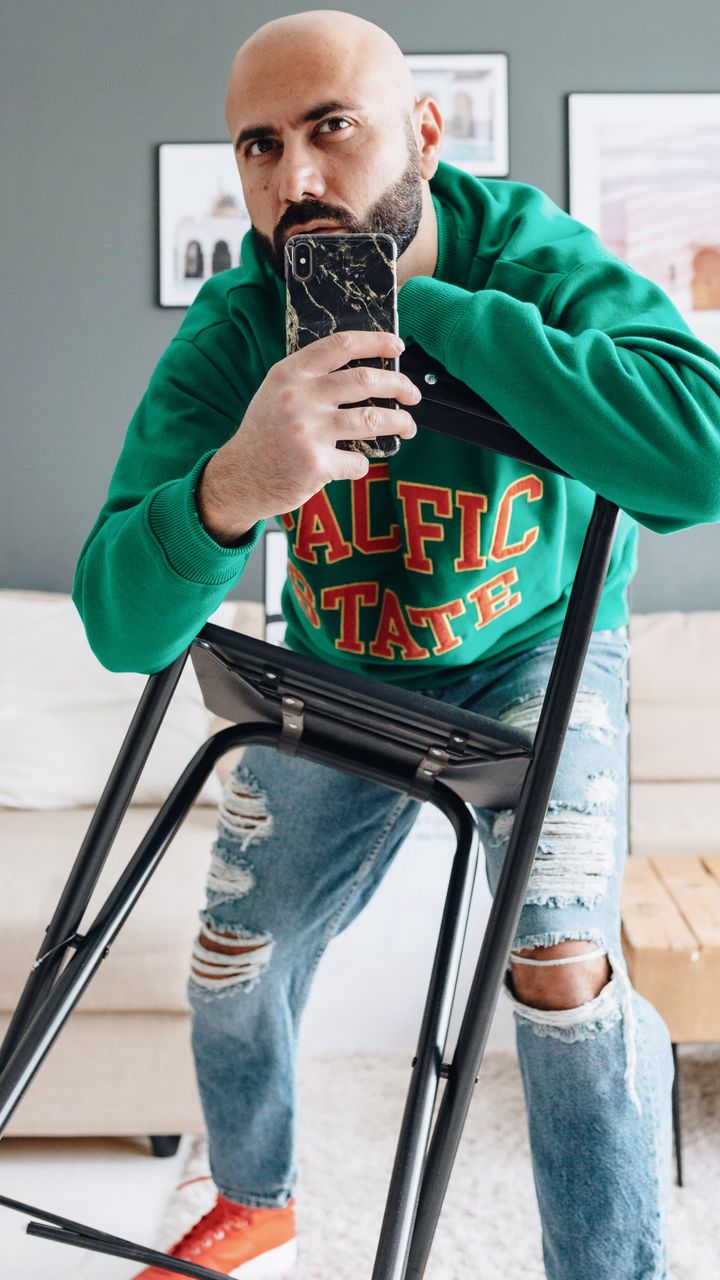 Man in a green sweatshirt taking a mirror photo at home